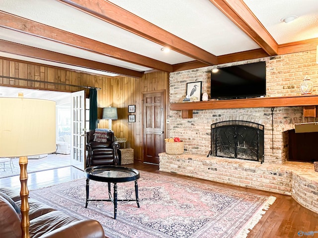 living area with a textured ceiling, wood walls, beamed ceiling, a fireplace, and wood finished floors