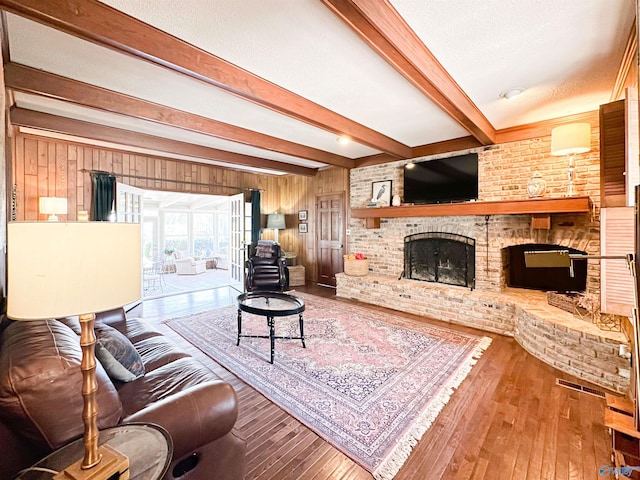 living area with hardwood / wood-style flooring, a fireplace, wood walls, a textured ceiling, and beamed ceiling