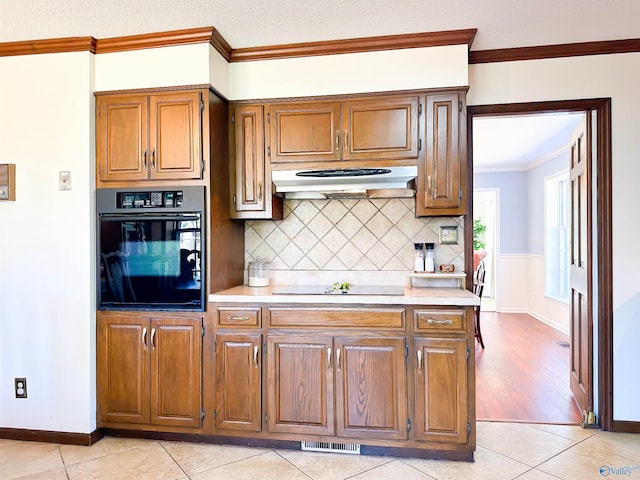 kitchen featuring light countertops, under cabinet range hood, ornamental molding, and black appliances