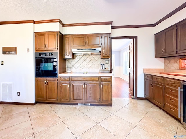 kitchen with light countertops, visible vents, crown molding, under cabinet range hood, and black appliances