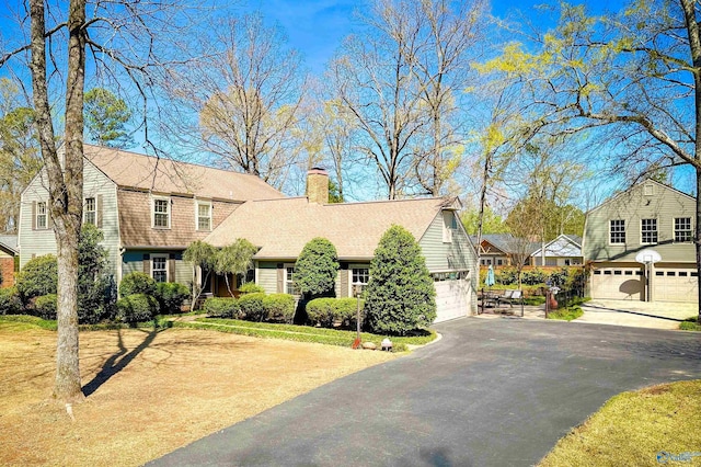 view of front facade with a chimney, roof with shingles, an attached garage, and aphalt driveway