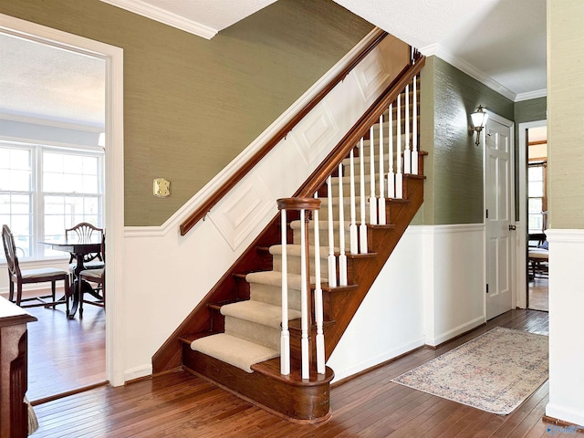 staircase featuring hardwood / wood-style floors, a wainscoted wall, ornamental molding, and a decorative wall