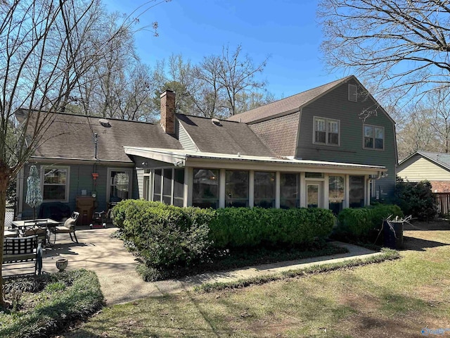 back of property with a gambrel roof, a sunroom, roof with shingles, a patio, and a chimney