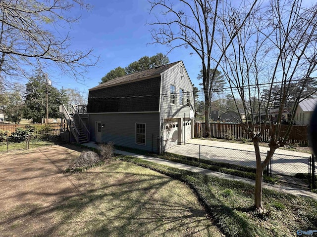 view of side of property featuring a gambrel roof, stairway, concrete driveway, fence, and a garage