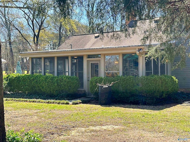 view of front facade with a sunroom, roof with shingles, and a front lawn