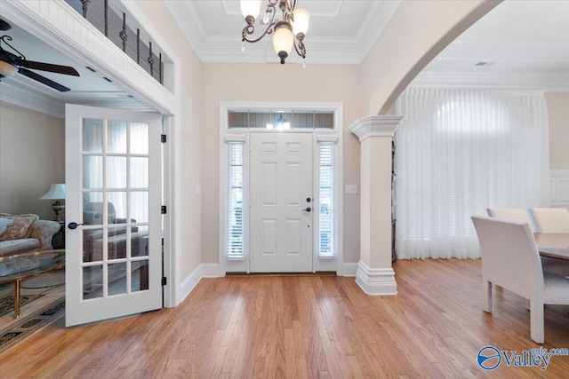 foyer entrance featuring light hardwood / wood-style flooring, ornate columns, a wealth of natural light, and ornamental molding