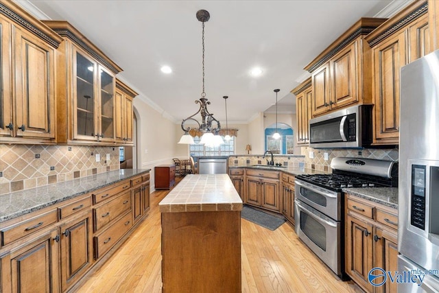 kitchen featuring decorative light fixtures, a kitchen island, sink, ornamental molding, and appliances with stainless steel finishes