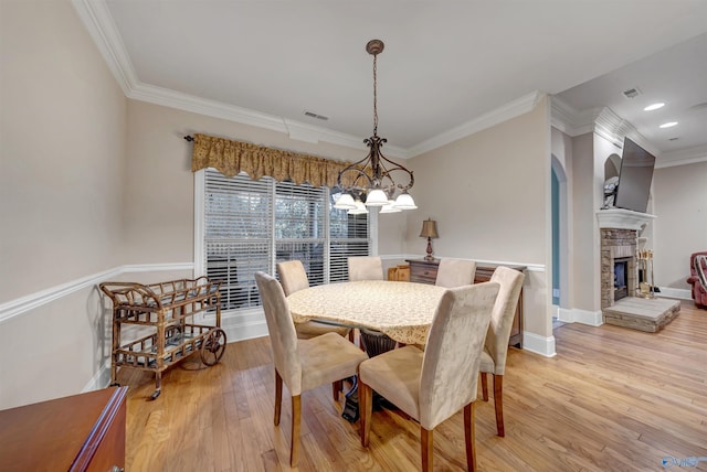 dining room featuring a stone fireplace, ornamental molding, and light hardwood / wood-style floors