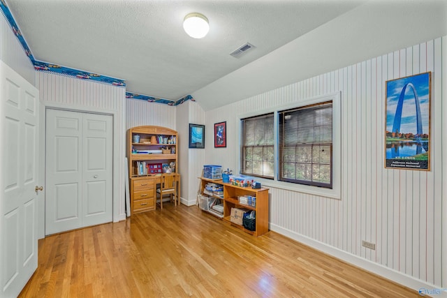 misc room with a textured ceiling, light hardwood / wood-style flooring, wood walls, and built in shelves