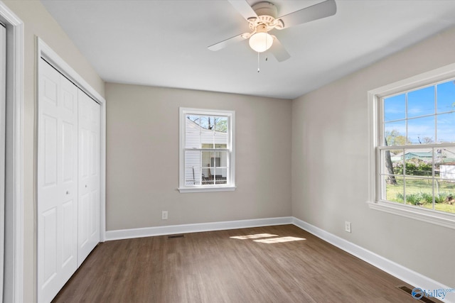 unfurnished bedroom featuring dark wood-style floors, a closet, baseboards, and multiple windows