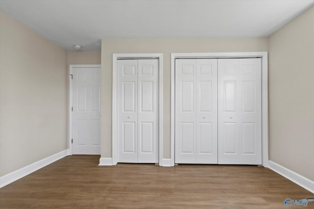unfurnished bedroom featuring baseboards, two closets, and wood finished floors
