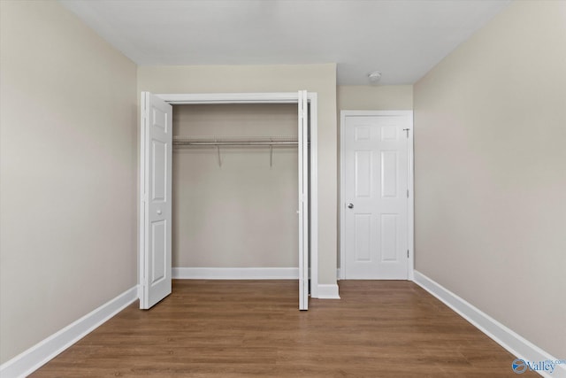 unfurnished bedroom with wood finished floors, baseboards, and a closet