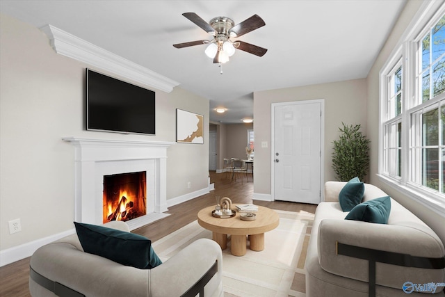 living area with a fireplace with flush hearth, wood finished floors, baseboards, and a ceiling fan