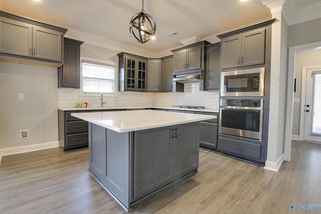 kitchen featuring gray cabinetry, under cabinet range hood, appliances with stainless steel finishes, decorative backsplash, and crown molding