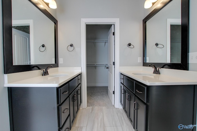 full bath with a spacious closet, two vanities, and a sink