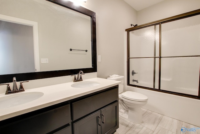 bathroom featuring toilet, double vanity, bath / shower combo with glass door, and a sink