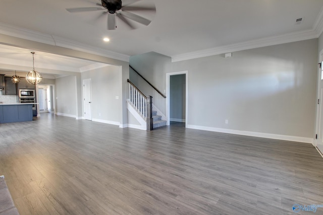 unfurnished living room with dark wood-style floors, stairway, ornamental molding, baseboards, and ceiling fan with notable chandelier