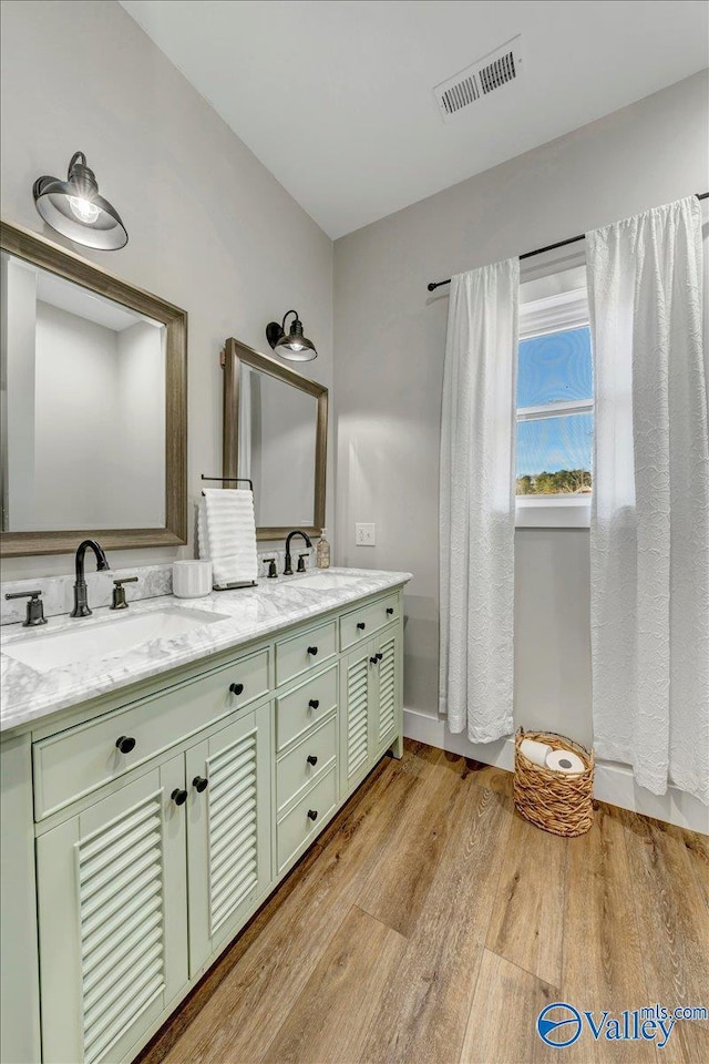 full bathroom featuring double vanity, visible vents, a sink, and wood finished floors