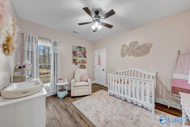 bedroom featuring visible vents, light wood-style flooring, a ceiling fan, a crib, and baseboards