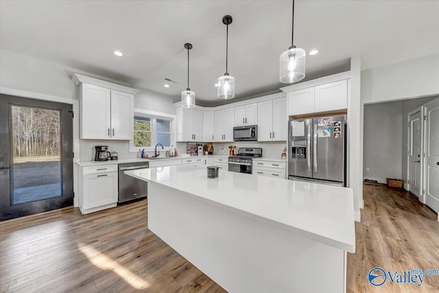 kitchen featuring pendant lighting, light countertops, appliances with stainless steel finishes, white cabinets, and a kitchen island