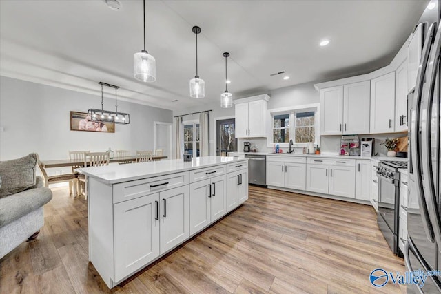 kitchen with light countertops, hanging light fixtures, light wood-style flooring, appliances with stainless steel finishes, and white cabinets