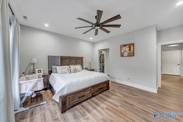 bedroom with a walk in closet, light wood finished floors, recessed lighting, visible vents, and baseboards