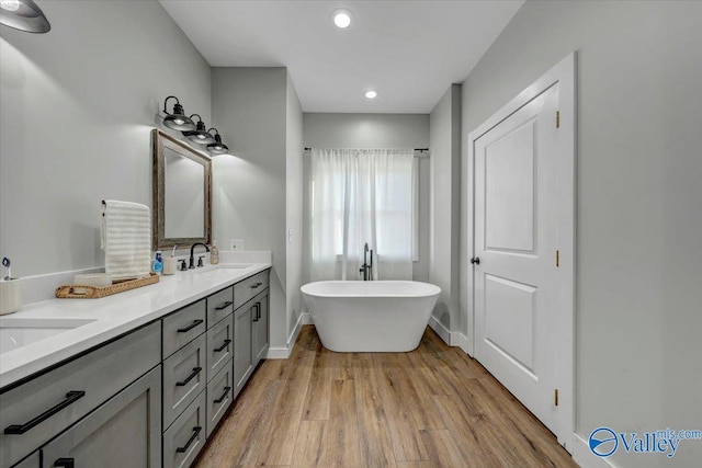 full bathroom with double vanity, baseboards, wood finished floors, a freestanding tub, and a sink