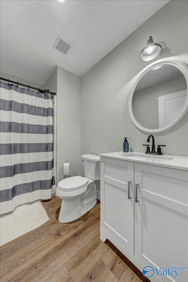 full bath featuring toilet, visible vents, wood finished floors, and vanity