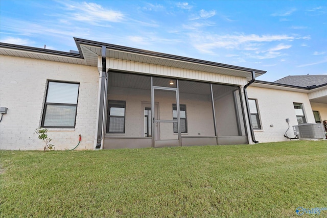 rear view of house with central air condition unit, a sunroom, and a lawn