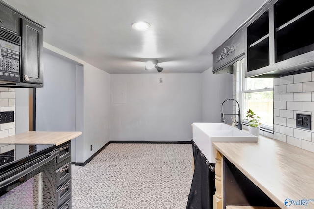 kitchen featuring black appliances, a sink, tasteful backsplash, baseboards, and dark cabinets