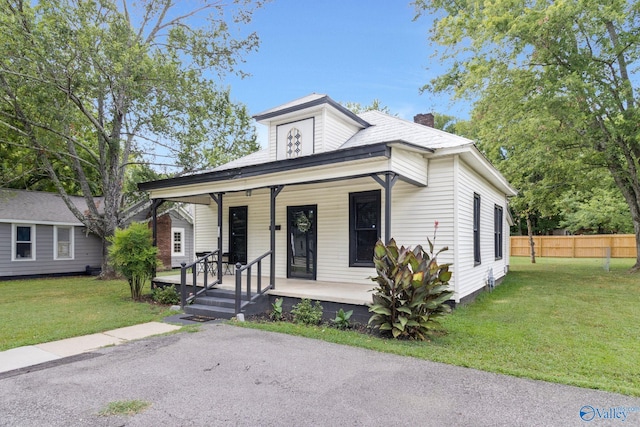 bungalow-style house with covered porch, a chimney, a front lawn, and fence