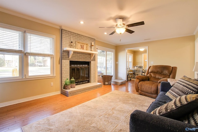 living room featuring hardwood / wood-style floors, ornamental molding, a brick fireplace, and ceiling fan