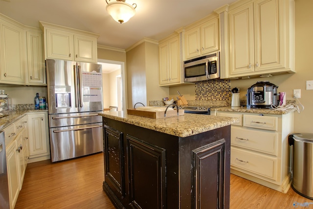 kitchen with a kitchen island with sink, stainless steel appliances, light stone countertops, ornamental molding, and light wood-type flooring