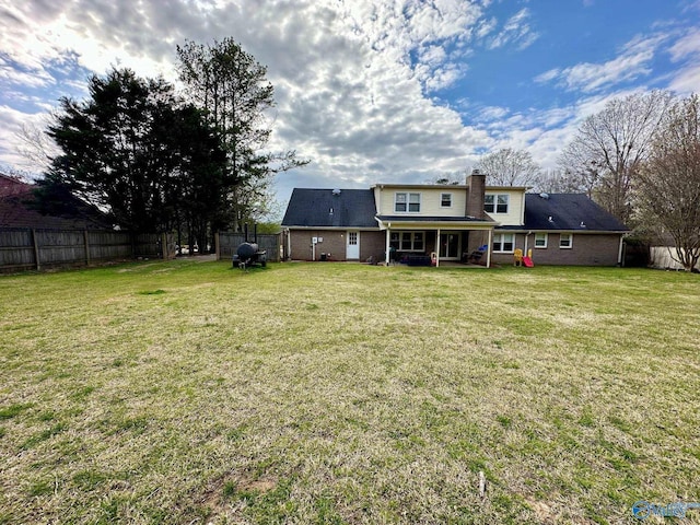 back of house featuring a fenced backyard, a chimney, brick siding, and a yard
