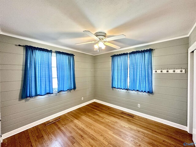 spare room with wooden walls, a textured ceiling, ceiling fan, and wood-type flooring