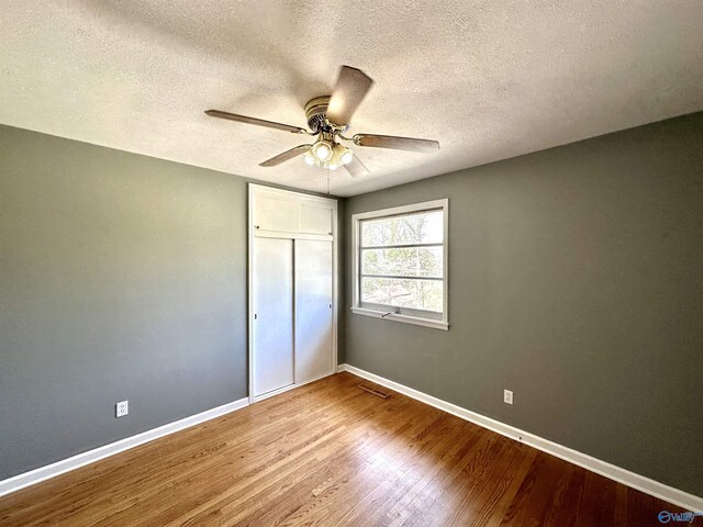 unfurnished bedroom with a textured ceiling, a closet, light wood-type flooring, and ceiling fan