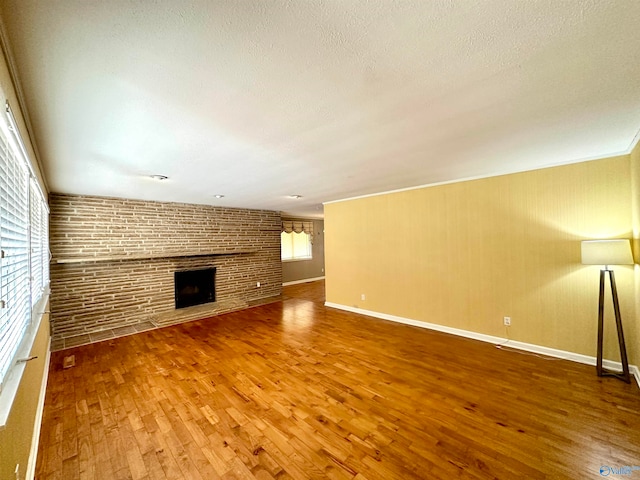 unfurnished living room with brick wall, a fireplace, a textured ceiling, and hardwood / wood-style floors