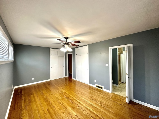 unfurnished bedroom featuring baseboards, two closets, visible vents, and light wood-style floors