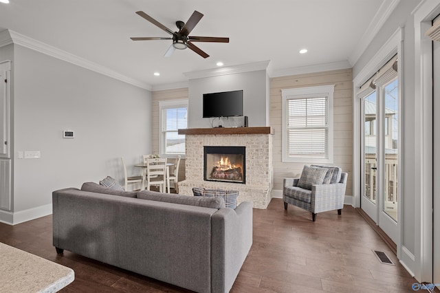 living area with dark wood-type flooring, a brick fireplace, visible vents, and crown molding