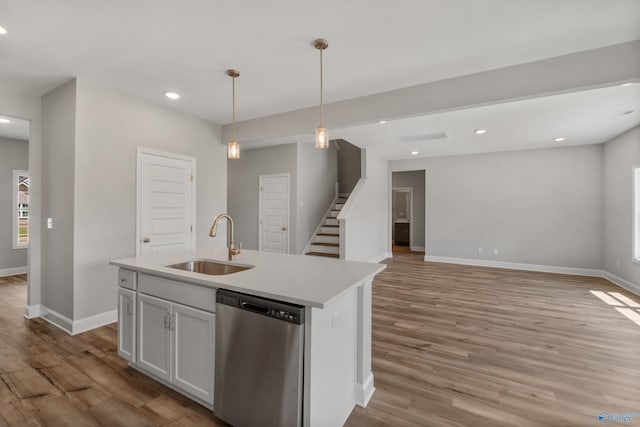 kitchen featuring light hardwood / wood-style floors, stainless steel dishwasher, sink, a center island with sink, and pendant lighting