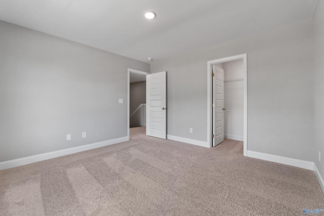 unfurnished bedroom with a walk in closet, a closet, and light carpet