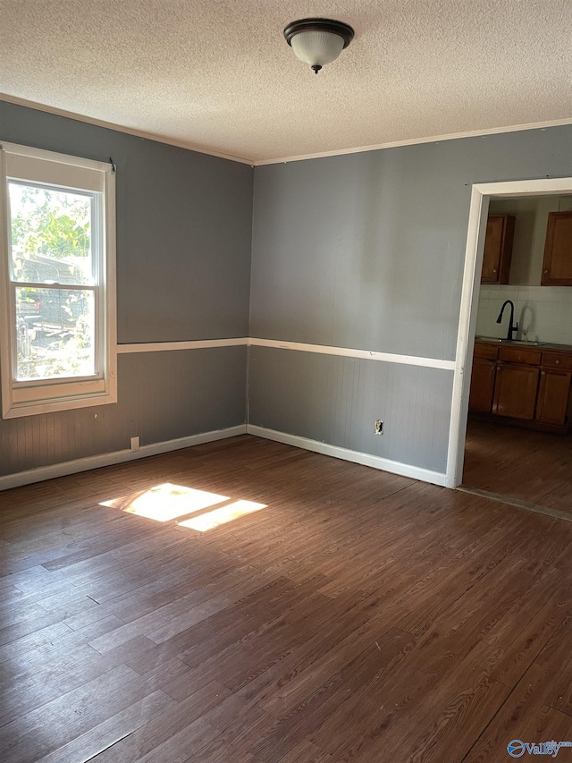 empty room with a textured ceiling, ornamental molding, and dark wood-type flooring