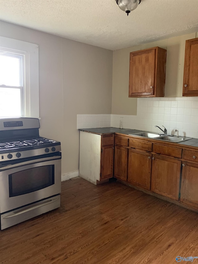 kitchen featuring stainless steel gas stove, tasteful backsplash, dark wood-type flooring, and sink