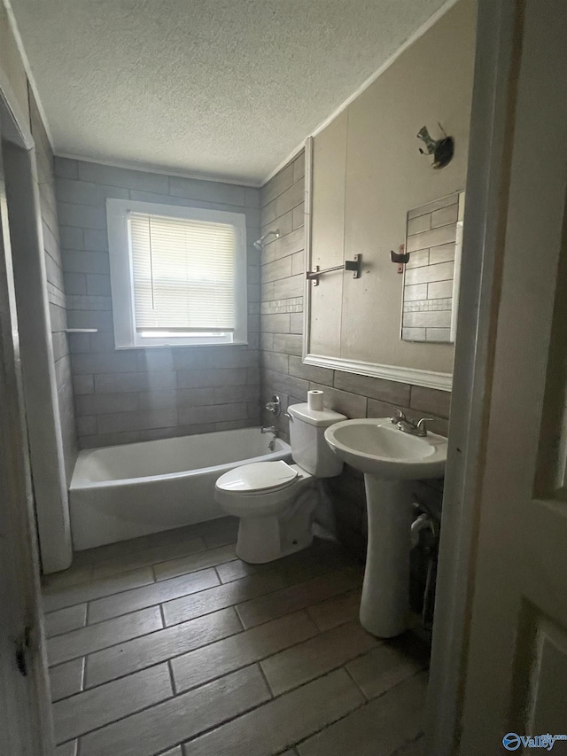 bathroom featuring tiled shower / bath combo, toilet, wood-type flooring, and a textured ceiling