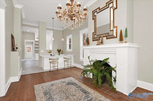 living room with a brick fireplace, dark hardwood / wood-style floors, ornamental molding, and a chandelier