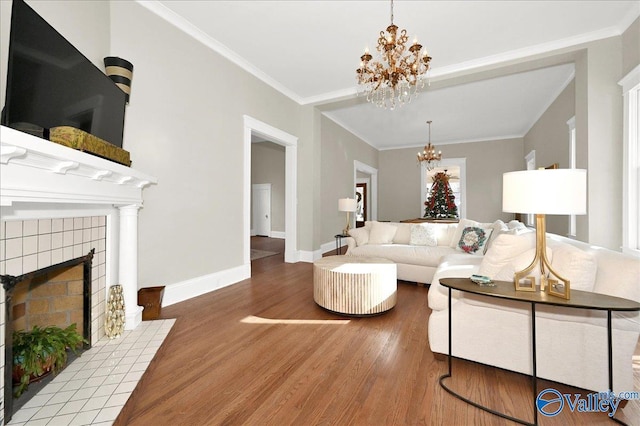 living room with a fireplace, wood-type flooring, ornamental molding, and a notable chandelier