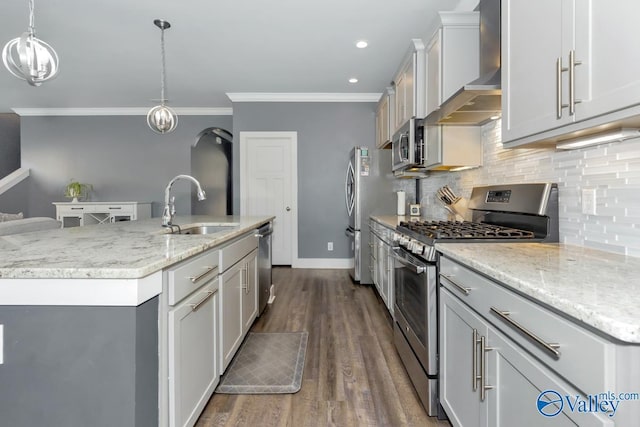 kitchen featuring a kitchen island with sink, stainless steel appliances, a sink, wall chimney range hood, and decorative backsplash