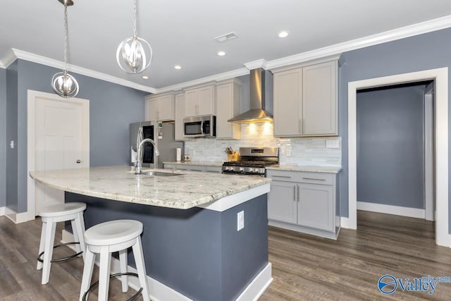 kitchen with appliances with stainless steel finishes, a breakfast bar, a kitchen island with sink, gray cabinets, and wall chimney range hood