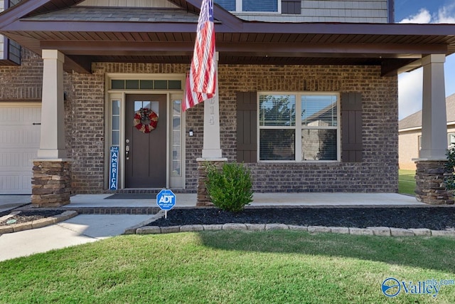 view of exterior entry with a garage, brick siding, and a porch