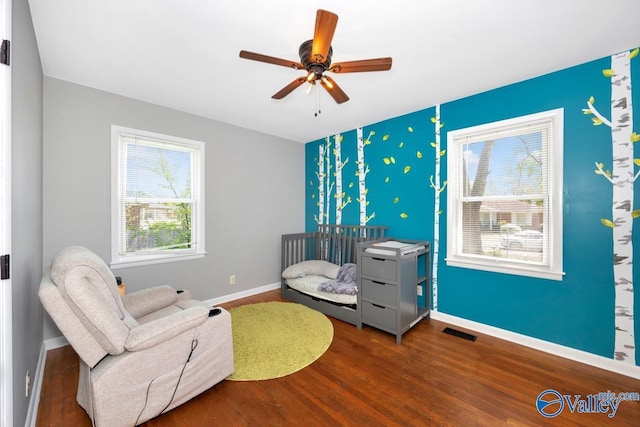 living area with a ceiling fan, an accent wall, wood finished floors, baseboards, and visible vents
